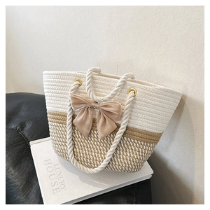 Detail of woven straw tote bag with cotton handles and a pink ribbon bow on a white book