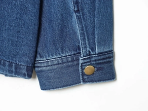 Dettaglio giacca di jeans blu scuro con bottoni in metallo dorato e doppie cuciture