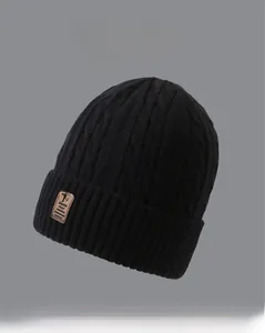 Close-up of thick cable knit texture on a black winter beanie with a brown leather patch