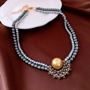 Détail d'un collier de perles grises avec pendentif fleur dorée et strass colorés