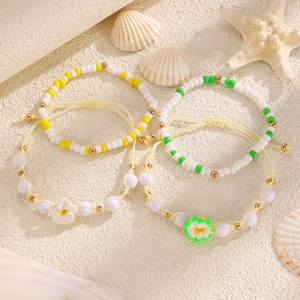 Dettaglio di quattro braccialetti di perline fatti a mano con fiori di plumeria e temi marini