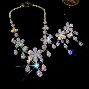 Close-up of sparkling floral pendant and droplet tassel earrings set on a dark surface