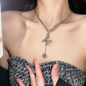 Detail of silver asymmetric necklace with H-letter pendant and sparkling rhinestones