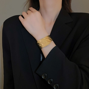 Close-up of a wide hammered gold cuff bracelet on a model wearing a black blazer