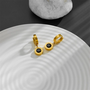 Close-up of gold titanium steel hoop earrings with Roman numerals and black stone inlay