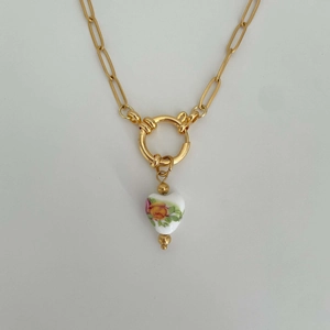 Close-up of golden necklace featuring a white heart pendant with rose floral patterns