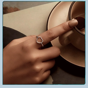 Close-up of silver heart-shaped open ring worn on finger with a cozy coffee cup backdrop
