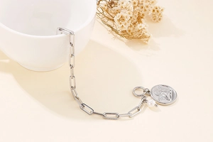 Close-up of silver chain bracelet with angel coin pendant and a single pearl accent