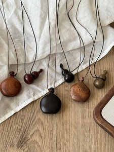 Macro detail of hand-polished wooden gourd and vase pendants on minimalist cotton fabric