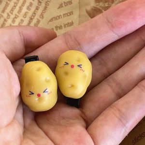 Detailed view of realistic potato hair clips with funny faces held in hand for size