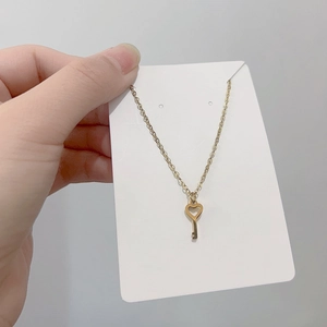 Macro shot of a golden heart-shaped key pendant necklace held on a minimalist white card