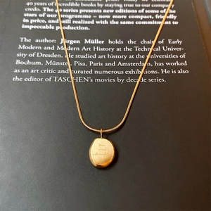 Detail of gold titanium necklace with 'you are adorable' engraved oval pendant on a book