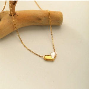 Detailed close-up of a gold heart pendant with white shell inlay on a natural wood branch
