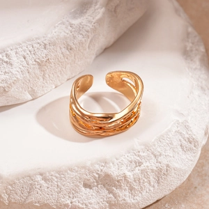 Dettaglio dell'anello d'oro regolabile con trama ondulata su blocchi di pietra bianca