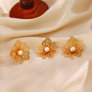 Elegant gold hollow flower earrings with white pearl centers on silk fabric