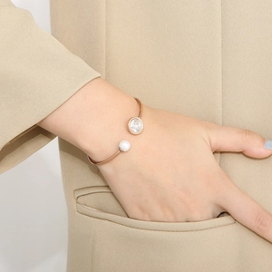 Bracelet jonc or rose avec perle blanche et zircon porté sur une veste de couleur kaki