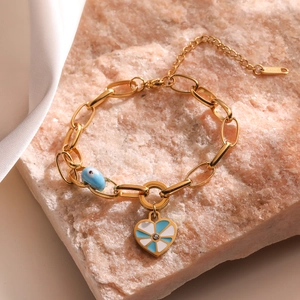 Detail of gold stainless steel bracelet featuring blue evil eye bead and enamel heart charm