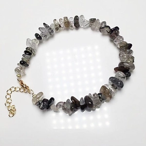 Macro detail of natural black rutilated quartz beaded bracelet with golden lobster clasp