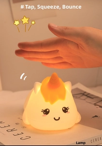 Close-up of hand tapping a soft silicone unicorn night light with warm yellow glow