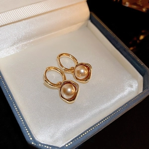 Gros plan macro de boucles d'oreilles perles dorées sur une doublure en soie blanche