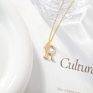 Detail of gold letter R necklace featuring a small flower with sparkling zircon stone