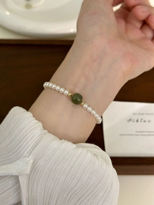 Detail of elegant pearl bracelet with green jade bead and gold spacers on female wrist