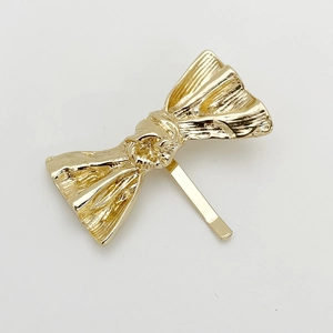 Detail of a minimalist gold metal bow hair hook with a polished textured finish