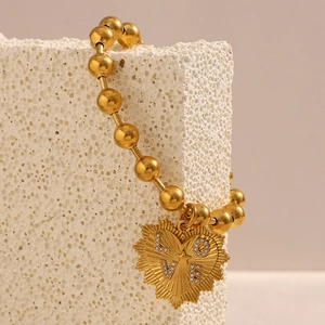 Dettaglio del bracciale con perline dorate e ciondolo a cuore LOVE su roccia bianca