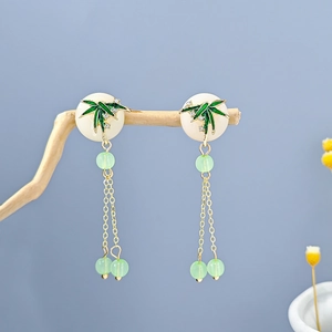 Macro shot of vintage long tassel earrings with green bamboo leaves on dry wooden branch