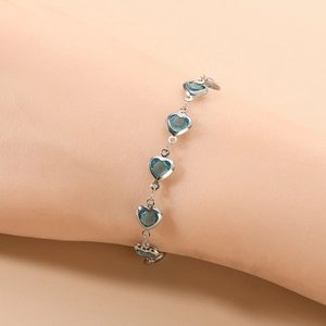 Détail d'un bracelet cœur argenté avec pierres en verre bleues au poignet d'un modèle