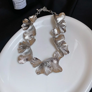 Macro detail of silver floral petal pendant necklace with textured finish on white tray