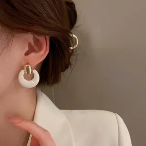 Elegant white circular drop earrings with gold metal studs on a female model