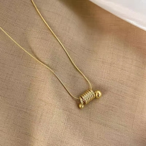 Golden spring spiral pendant on a fine snake chain necklace displayed on beige fabric