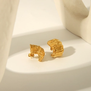Gros plan de boucles d'oreilles créoles dorées avec texture spirale en acier titane