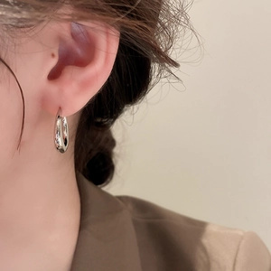 Side view of a model wearing minimalist silver C-shaped metal hoop earrings with a glossy finish