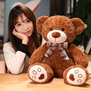 Cute dark brown teddy bear plush toy with a plaid bow tie shown with a model