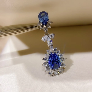 Detail of luxury teardrop earring with blue gems and clear crystals held by tweezers