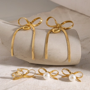 18K gold plated stainless steel bow earrings with tassel and pearl accents on stone stand