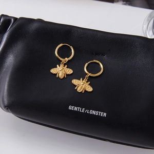 Golden bee hoop earrings with turquoise details on a textured leather surface