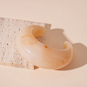 Detail view of a vintage acrylic C-shaped cuff bracelet with amber marble texture on stone