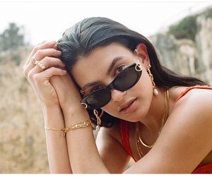 Close-up of retro black oval sunglasses paired with gold jewelry on a stylish model