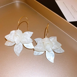 Detail of white resin flower earrings with gold hooks on a textured jewelry tray