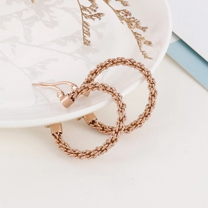 Détail de créoles tressées en or rose posées sur une assiette en céramique blanche