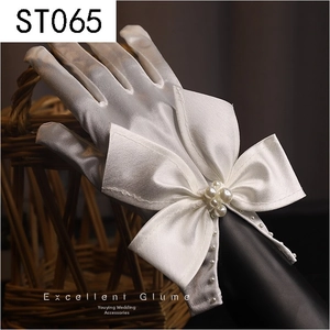 Close-up of white satin bridal gloves with lace, large bow, and pearl embellishments