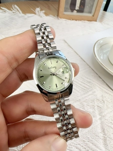 Close-up of a silver watch with light green dial and date display held in hand