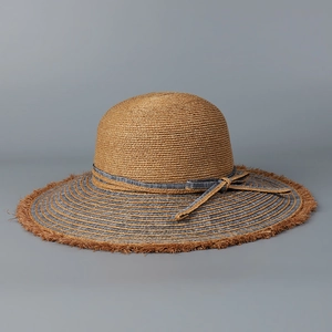 Detail of raffia sun hat featuring raw fringe edges and a striped denim bow band
