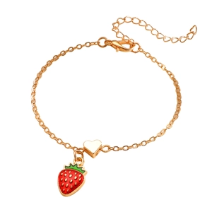 Dettaglio di un bracciale dorato con ciondolo a fragola rossa e cuore in metallo lucido