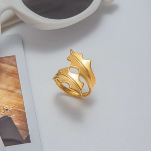 Détail d'une bague feuille dorée ajustable sur fond gris avec des accessoires