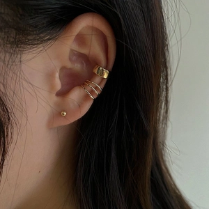 Close-up of minimalist gold cuff earrings and ball stud on a female ear