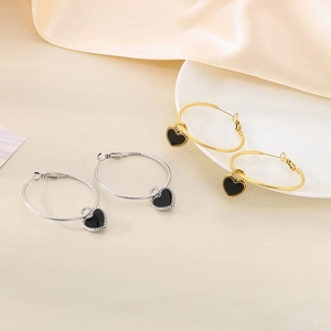 Golden and silver twisted hoop earrings with black enamel heart charms on silk fabric